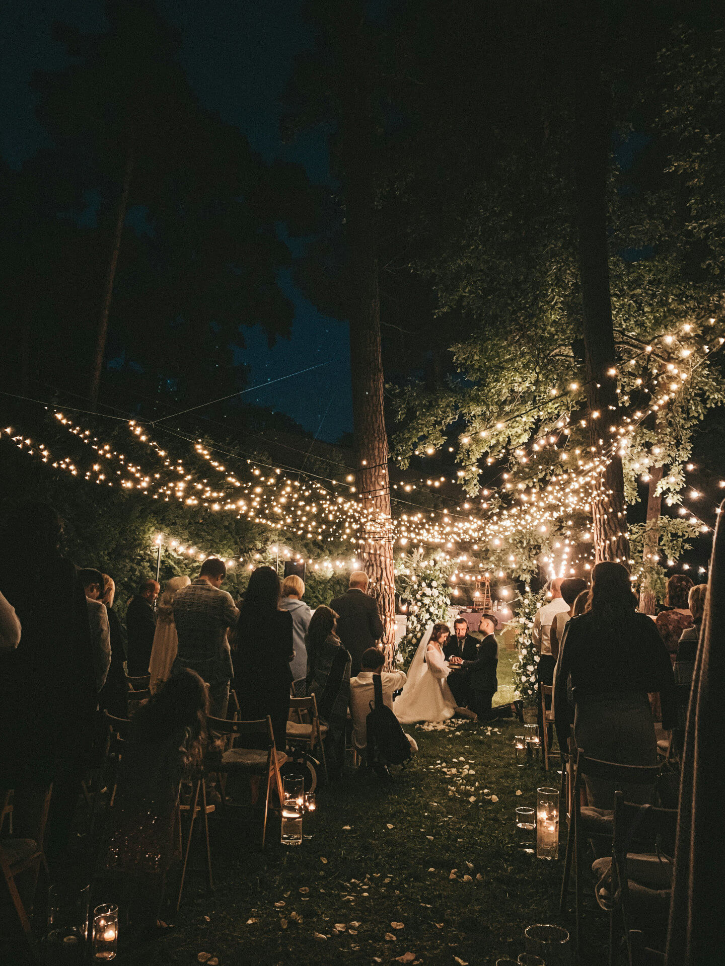 An evening ceremony under festoon lights in a woodland clearing