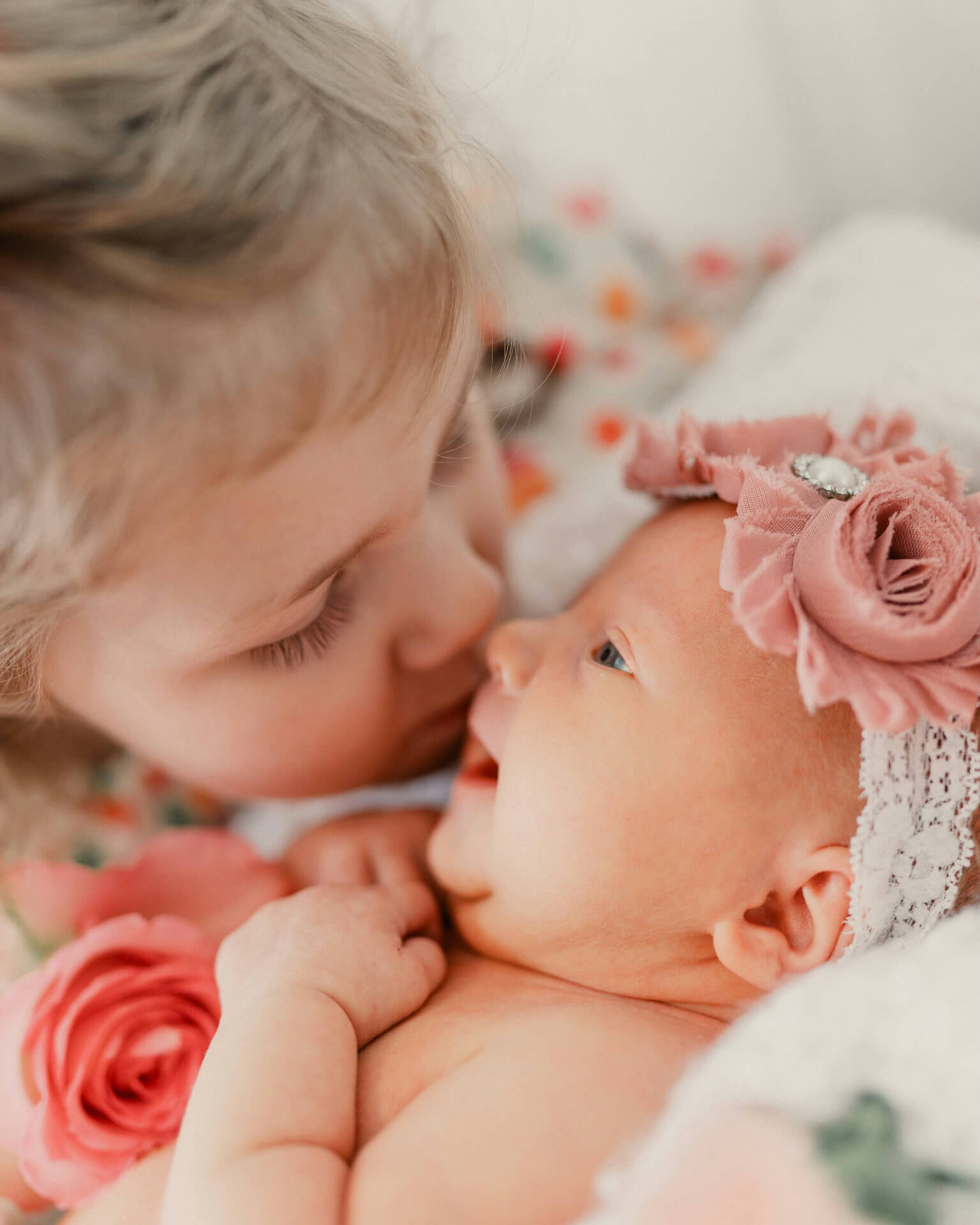 A small girl leaning in to kiss her newborn sibling