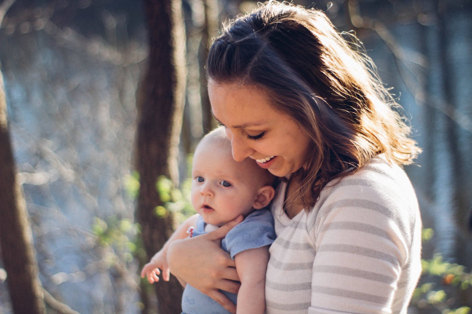A mother holding her baby outdoors in dappled woodland light
