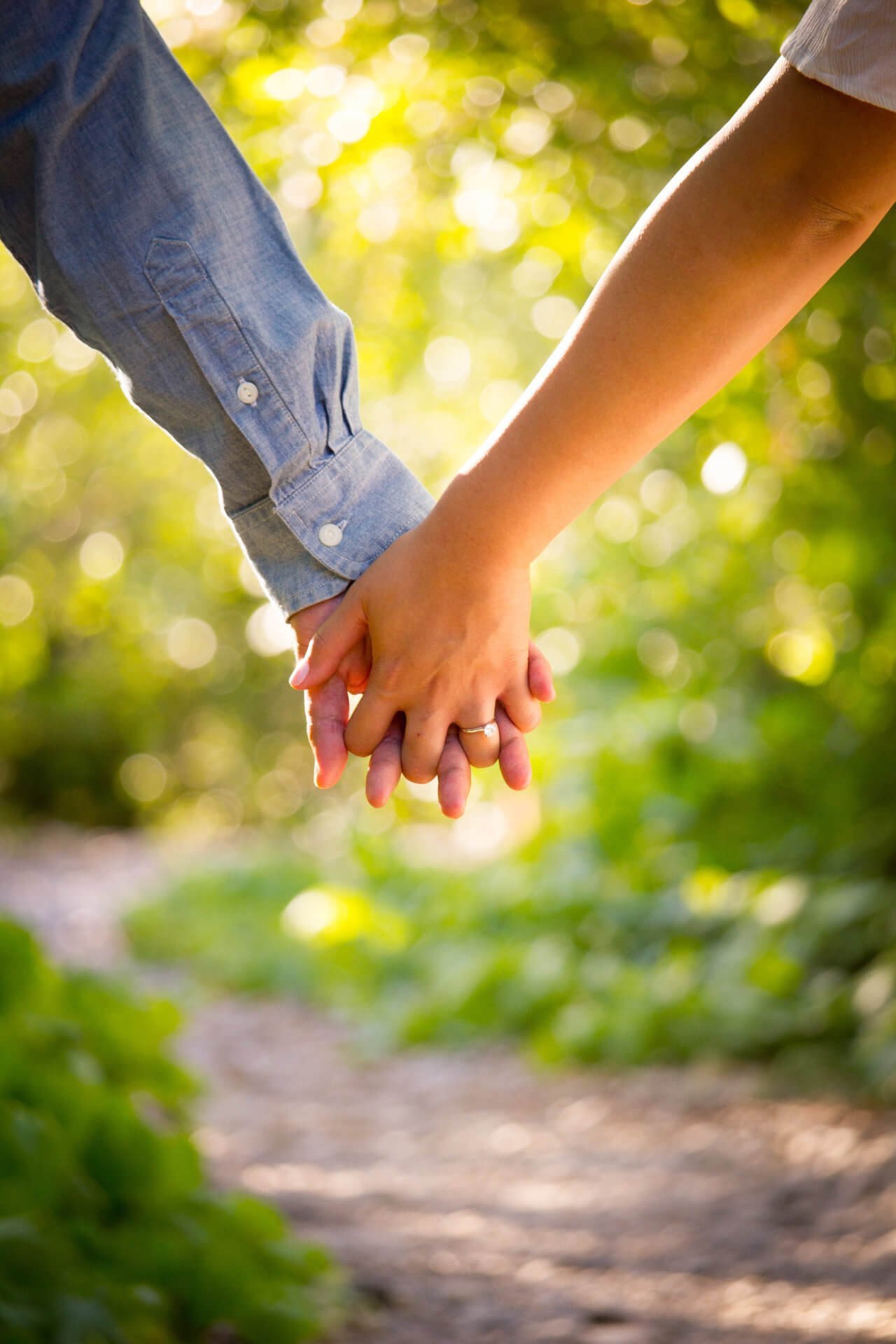 Two people holding hands as they walk a sunlit woodland path in summer